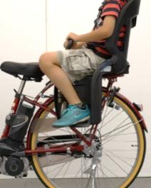 Photo of a child seated on a child bike seat. The photo shows a boy aged 9 when his feet are on the footrest