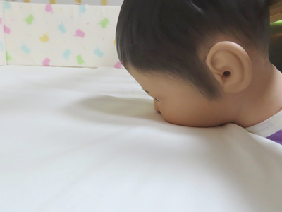 Photo of a baby dummy facing down on a crib with the head caught in a gap and the mouth and nose pressed against the mattress
