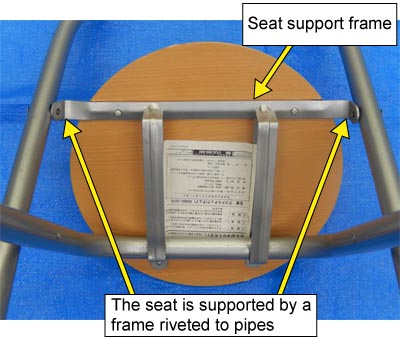 Photo of the underside of the seat supported by a frame. The frame is riveted to pipes to support the seat.