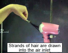 Photo of a scene when strands of artificial hair are drawn into the air inlet of a hair dryer
